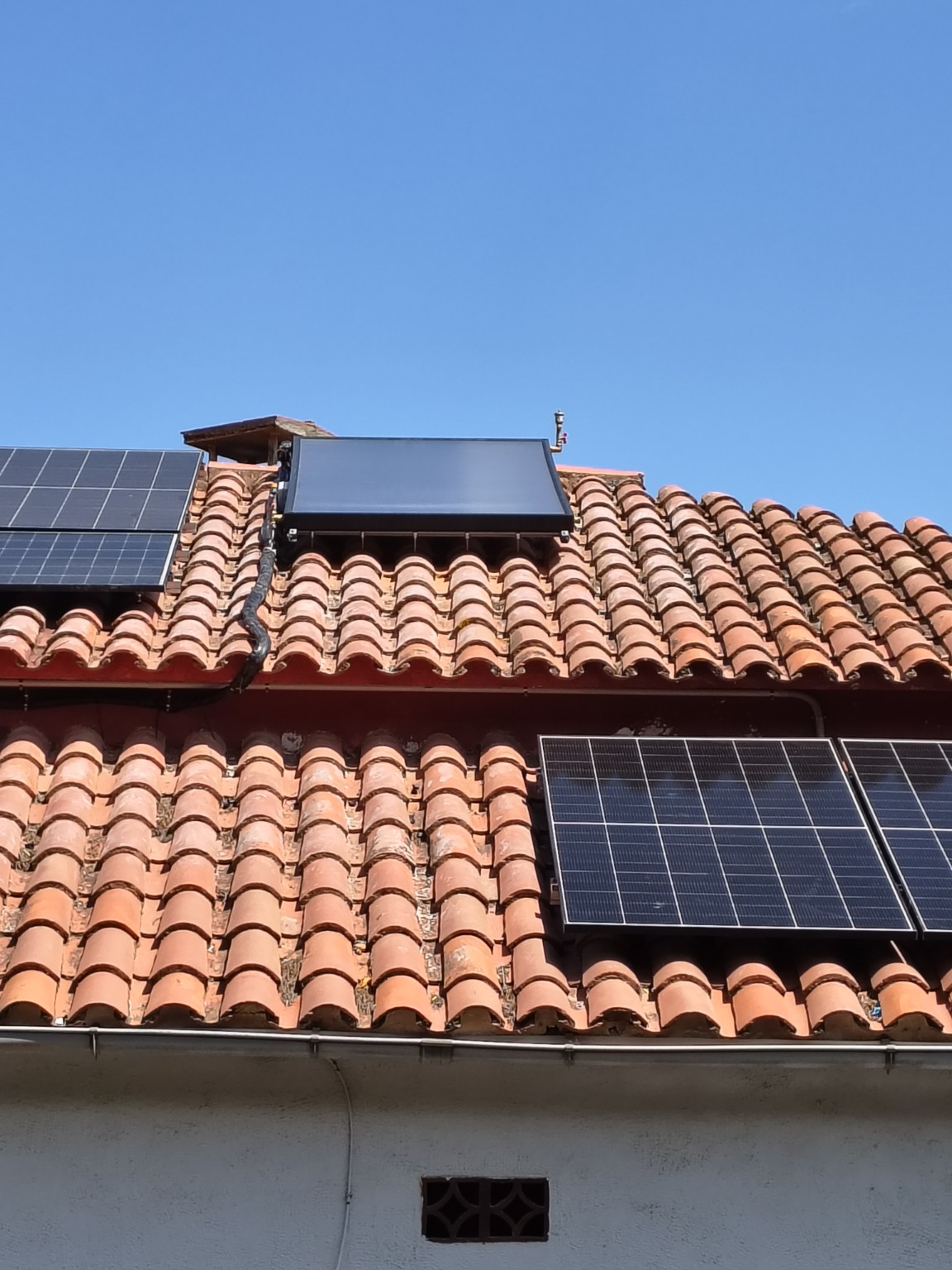 Solar thermal collector installed on a tiled roof beside photovoltaic panels